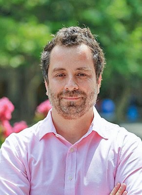 Portrait of Matías Negrete Pincetic outdoors, smiling with a pink shirt, in a green garden setting.