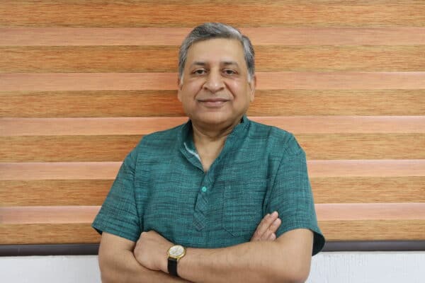 Shreekant Gupta, leader at Reset Network, standing confidently with arms crossed against a wooden ba.