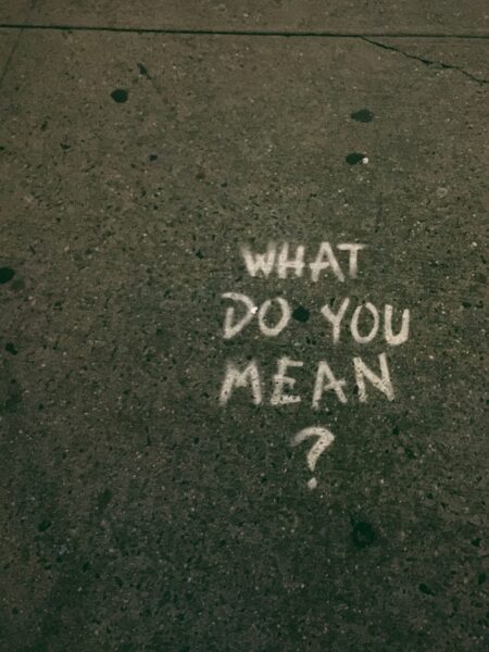 Chalk writing on pavement asking "What do you mean?" for clear messaging.