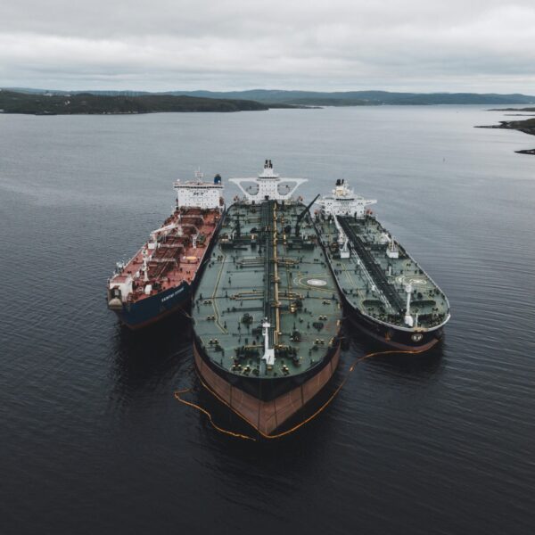 Three large red tankers off a coast in a calm sea. Two are slightly smaller and flank the largest.