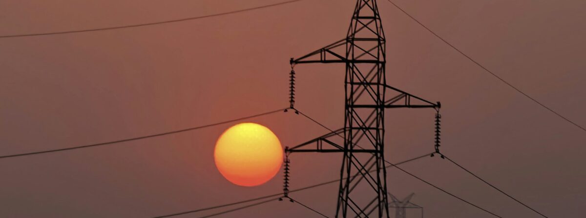 A red sun rises over a pinkish brown sky at dawn behind a large electricity transmission line tower