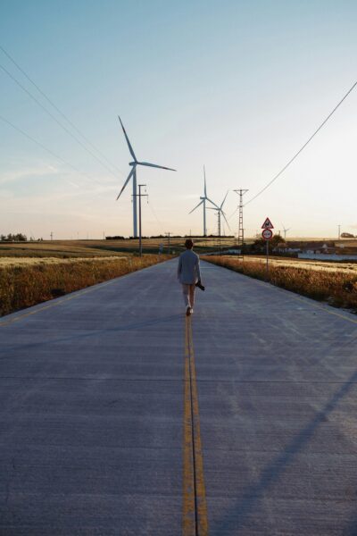 Person walking on road with wind turbines in the background at sunset.